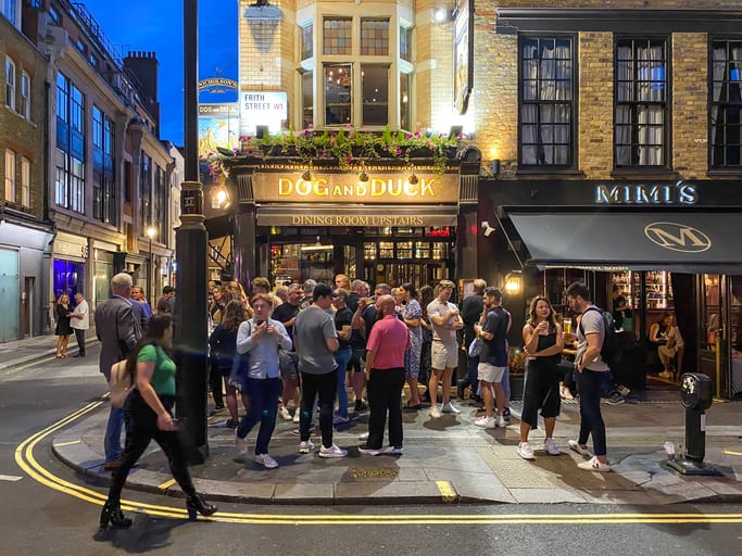 People drinking outside a traditional pub in the heart of London at night.